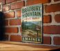 A vintage metal sign for Bradbury Mountain State Park in Maine, featuring a scenic landscape with pine trees and mountains.