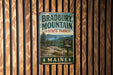 A vintage metal sign for Bradbury Mountain State Park in Maine, featuring a scenic landscape with pine trees and mountains.