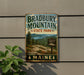 A vintage metal sign for Bradbury Mountain State Park in Maine, featuring a scenic landscape with pine trees, mountains, and a lake.
