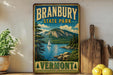 A vintage-style metal sign for Branbury State Park in Vermont, featuring a scenic landscape with a lake, mountains, and a sailboat.