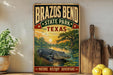 A vintage-style metal sign for Brazos Bend State Park in Texas, featuring an illustration of a crocodile in a pond with a sunset in the background.