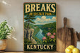 A vintage-style sign for Breaks Interstate Park in Kentucky, featuring a scenic landscape with a river, cliffs, and pink flowers.