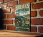 A vintage-style metal sign for "BREAKS INTERSTATE PARK" is displayed on a brick wall, featuring a scenic mountain landscape with a river and pine trees.