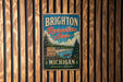 A vintage metal sign for Brighton Recreation Area in Michigan, featuring a scenic landscape with a lake, mountains, and pine trees.