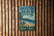 A vintage-style metal sign for Bristol Beach State Park in New York, featuring a beach scene with a sailboat and a wooden fence in the background.
