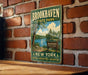 A vintage-style metal sign for Brookhaven State Park, featuring a scenic landscape with a lake and trees, mounted on a brick wall.