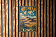 A vintage metal sign for Brunette Dunes State Park in Idaho, featuring a desert landscape with sand dunes and mountains in the background.
