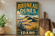 A vintage-style sign for Brunette Dunes State Park in Idaho, featuring a scenic illustration of sand dunes and mountains.