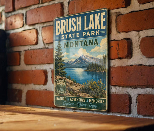 A vintage metal sign for Brush Lake State Park in Montana, featuring a scenic landscape with mountains, trees, and a lake.