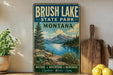 A vintage-style sign for Brush Lake State Park in Montana, featuring a scenic landscape with mountains, a lake, and pine trees.