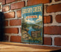 A vintage-style sign for Brushy Creek State Recreation Area in Iowa, featuring a scenic illustration of the area with a river, mountains, and a sign for outdoor activities.