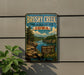 A vintage-style metal sign for Brushy Creek State Recreation Area in Iowa, featuring a scenic landscape with a river, mountains, and trees.