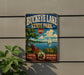 A vintage-style sign for Buckeye Lake State Park, featuring a scenic illustration of a lake, a sailboat, and a peaceful outdoor setting with a chair and flowers.