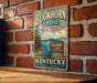 A vintage-style sign for Buckhorn Lake State Resort Park in Kentucky, featuring a scenic illustration of the lake surrounded by trees and mountains.