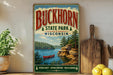 A vintage-style sign for Buckhorn State Park in Wisconsin, featuring a scenic landscape with a lake, mountains, and a canoe.