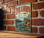 A vintage metal sign for Buckhorn State Park in Wisconsin, featuring a scenic landscape with a lake, mountains, and pine trees.