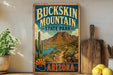 A vintage-style metal sign for Buckkin Mountain State Park in Arizona, featuring a desert landscape with a cactus and mountains in the background.
