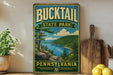 A vintage-style sign for Bucktail State Park in Pennsylvania, featuring a scenic landscape with a lake and mountains.