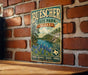 A vintage-style metal sign for Buescher State Park in Texas, featuring a scenic landscape with pine trees, a lake, and a trail.