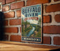 A vintage-style metal sign for Buffalo River State Park in Minnesota, featuring a scenic illustration of the river surrounded by lush greenery.