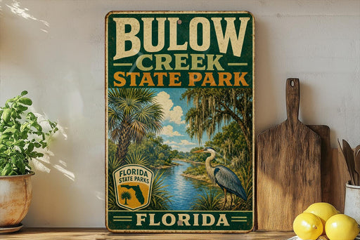 A vintage-style sign for Bulow Creek State Park in Florida, featuring a scenic illustration of a bird and palm trees, with a wooden paddle and a potted plant in the foreground.