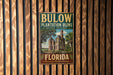 A vintage-style metal sign for Bulow Plantation Ruins Historic State Park in Florida, featuring a building and palm trees.