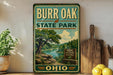 A vintage-style metal sign for Burr Oak State Park in Ohio, featuring a scenic landscape with a river and trees.