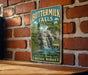 A vintage-style metal sign for Buttermilk Falls State Park, featuring a waterfall and lush greenery, is displayed on a brick wall.