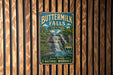 A vintage-style metal sign for Buttermilk Falls State Park, featuring a waterfall and lush greenery, is displayed on a wooden wall.
