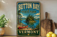 A vintage-style metal sign for Button Bay State Park in Vermont, featuring a scenic image of a lake, pine trees, and a canoe.