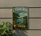 a vintage metal sign for Caesar Creek State Park in Ohio, depicting a scenic landscape with a lake, trees, and a sailboat.
