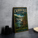 A vintage metal sign for Calhoun Falls State Park, featuring an illustration of a waterfall and lush greenery, is displayed on a gray countertop next to a stack of black camera lenses.