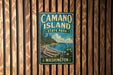 A vintage metal sign for Camano Island State Park in Washington, featuring a scenic landscape with a lake, trees, and a sailboat.