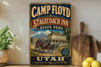 A vintage-style metal sign for Camp Floyd Stagecoach Inn in Utah, featuring an illustration of a stagecoach and a scenic mountain backdrop.