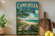 A vintage-style sign for Camp Helen State Park in Florida, featuring a beach scene with a wooden walkway leading to the beach.