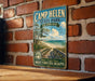 A vintage-style metal sign for Camp Helen State Park in Florida, featuring a scenic beach and palm trees, is displayed on a brick wall.