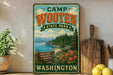 A vintage-style metal sign for Camp Wooten State Park in Washington, featuring a scenic landscape with a mountain, pine trees, and a cabin.