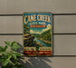A vintage-style metal sign for Cane Creek State Park in Arkansas, featuring a scenic landscape with a river and mountains.