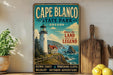A vintage-style poster of Cape Blanco State Park in Oregon, featuring a lighthouse and coastal landscape, is displayed on a wall next to a wooden cutting board and some lemons.