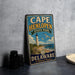 A vintage metal sign for Cape Henlopen State Park in Delaware, featuring a lighthouse and beach scene.