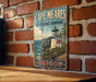 A vintage metal sign for Cape Meares State Scenic Viewpoint in Oregon, featuring a lighthouse and coastal landscape.