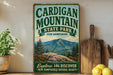 A vintage-style sign for Cardigan Mountain State Park in New Hampshire, featuring a scenic mountain landscape and the text "Explore, Discover, New Hampshire's Natural Beauty".