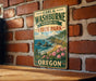 A vintage metal sign for Carl G. Washburne Memorial State Park in Oregon, featuring a scenic landscape with mountains, cliffs, and a body of water.