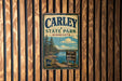 A vintage metal sign for Carley State Park in Minnesota, featuring a scenic landscape with pine trees, a lake, and mountains.
