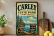 A vintage-style metal sign for Carley State Park in Minnesota, featuring a scenic landscape with pine trees, a lake, and a sign that says "Nature, Adventure, Memories".