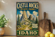 A vintage-style sign for Castle Rocks State Park in Idaho, featuring a scenic mountain landscape with pine trees and a winding path.