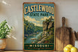 A vintage-style metal sign for Castlewood State Park in Missouri, featuring a scenic landscape with a river and rocky cliffs.