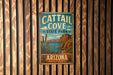 A vintage metal sign for Cattail Cove State Park in Arizona, featuring a desert landscape with mountains, cacti, and a body of water.