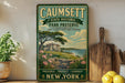 a vintage-style sign for Caumsett State Historic Park Preserve, which is located in Long Island's Gold Coast Heritage. The sign is displayed on a wooden shelf, surrounded by various kitchen utensils and a potted plant.