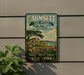 a vintage metal sign with a scenic illustration of a coastal landscape, including a house and trees, mounted on a wall.